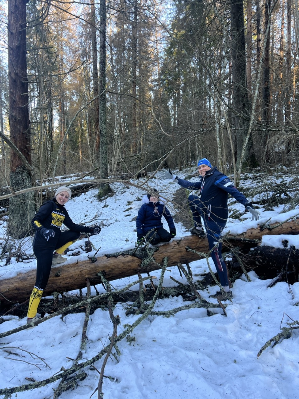 Kolm matkajat lumises metsas üle langenud puu ronimas